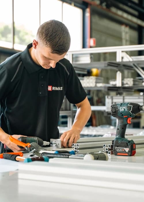 Rimas-medewerker monteert aluminium profielen met een accuschroefmachine in de werkplaats